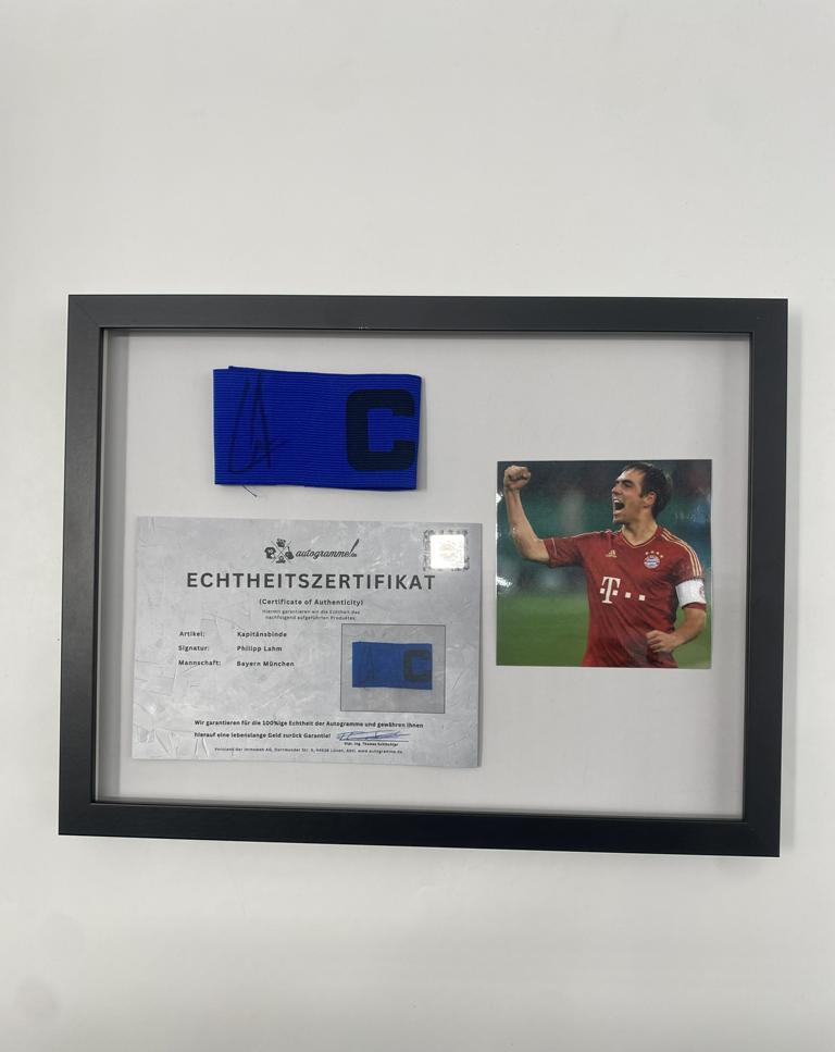 Brazalete de capitán firmado por Philipp Lahm en un marco de autógrafos del Bayern de Múnich.