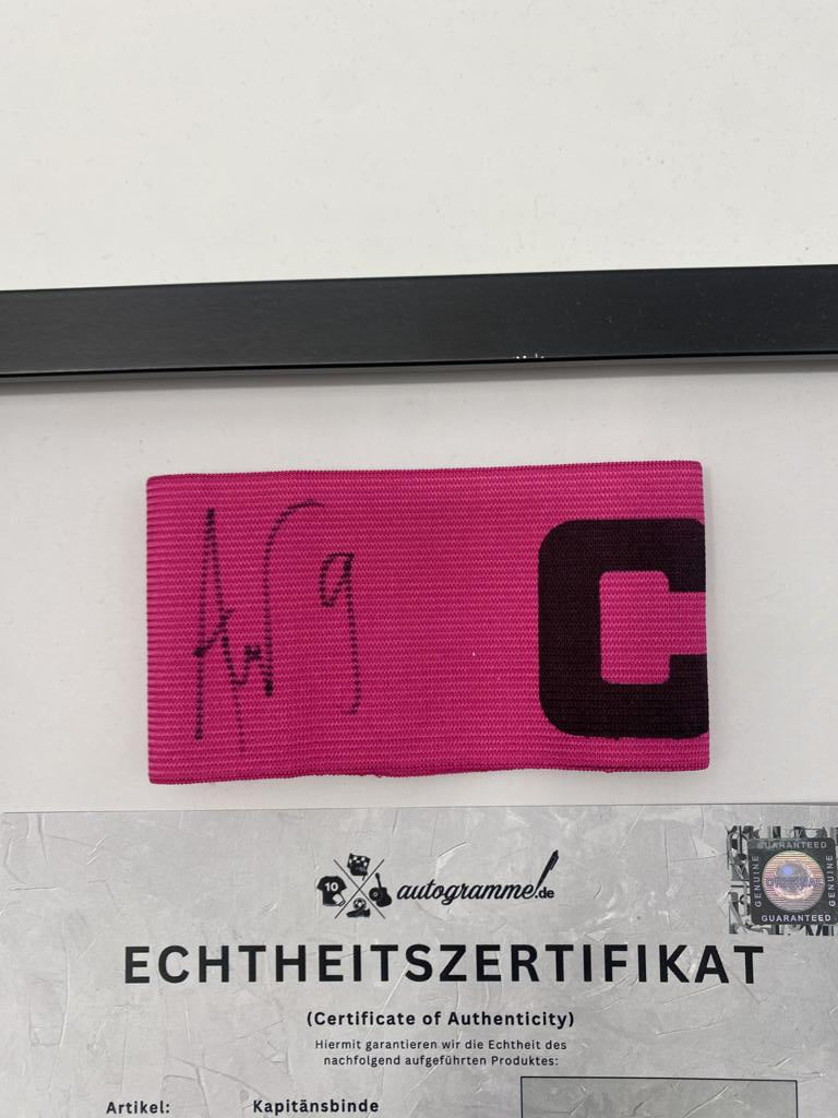 Brazalete de capitán firmado por Mohamed Amoura en un marco de Wolfsburg, certificado de autenticidad.