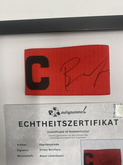 Kapitänsbinde Victor Boniface signiert im Rahmen Bayer Leverkusen Autogramm