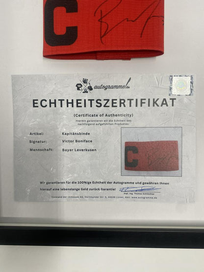 Kapitänsbinde Victor Boniface signiert im Rahmen Bayer Leverkusen Autogramm
