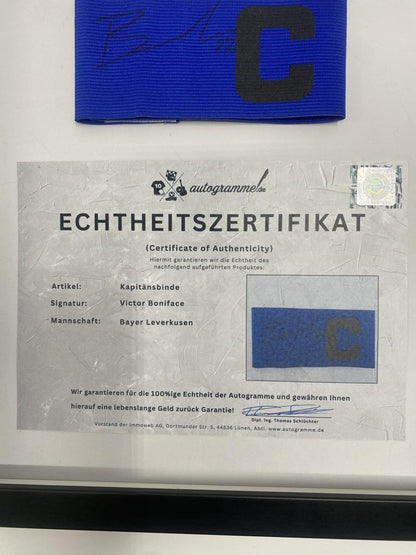 Kapitänsbinde Victor Boniface signiert im Rahmen Bayer Leverkusen Autogramm