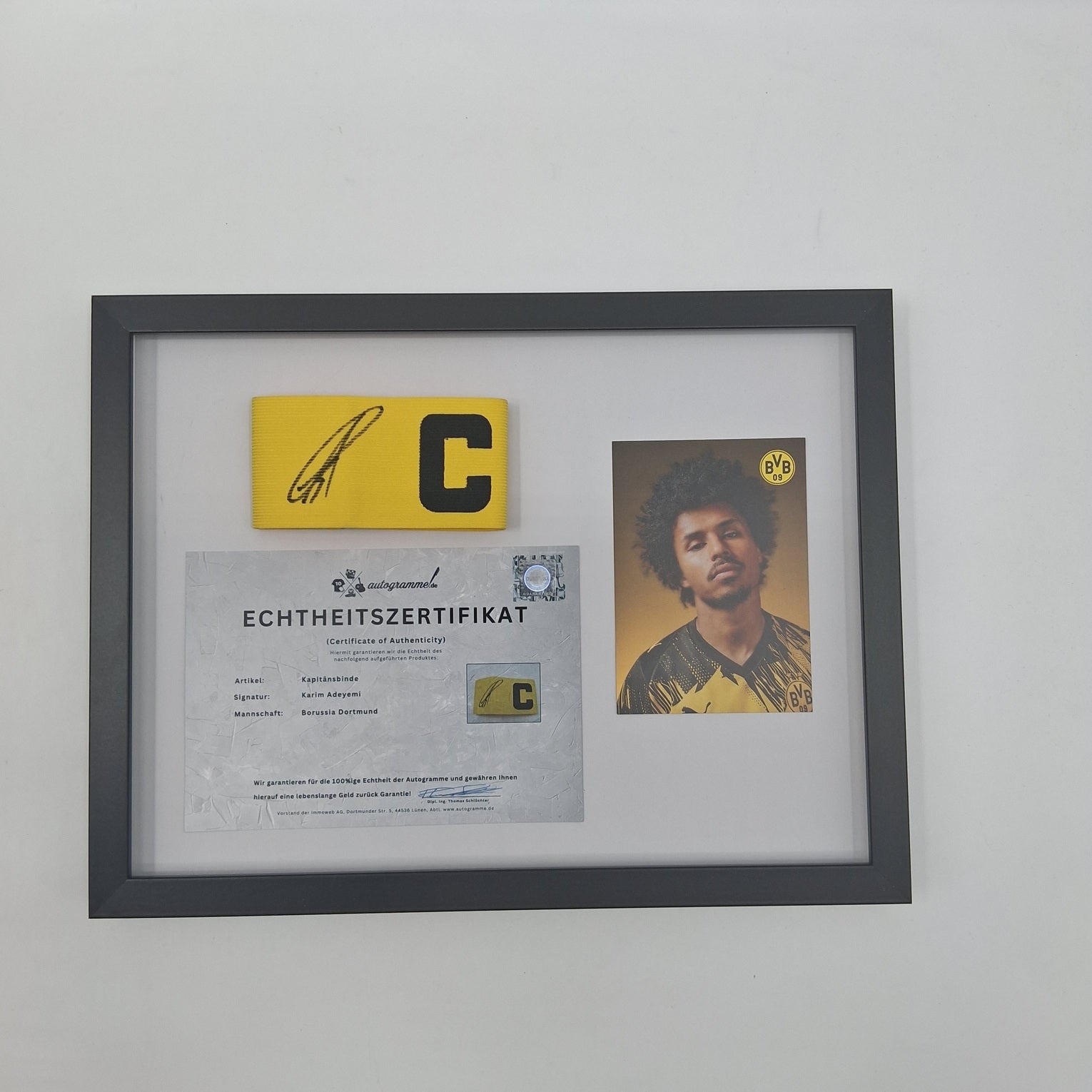 Brazalete de capitán firmado por Karim Adeyemi en un marco con certificado de autenticidad del Borussia Dortmund.