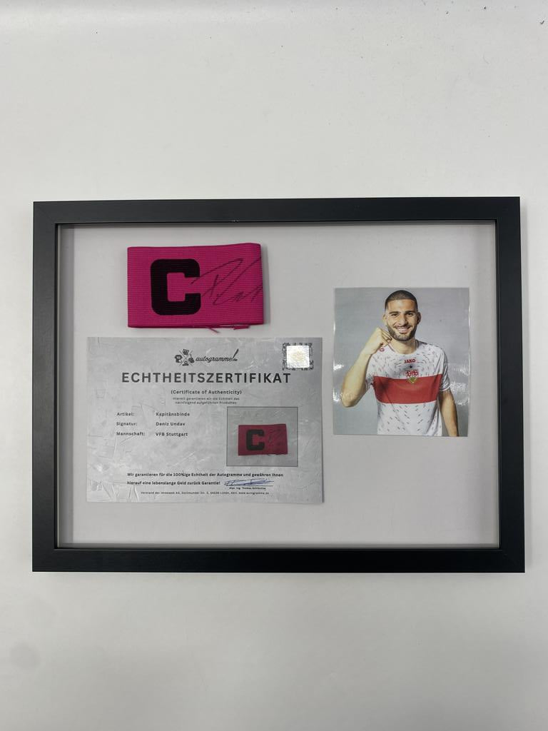 Brazalete de capitán firmado por Deniz Undav en un marco de autógrafos del VfB Stuttgart.