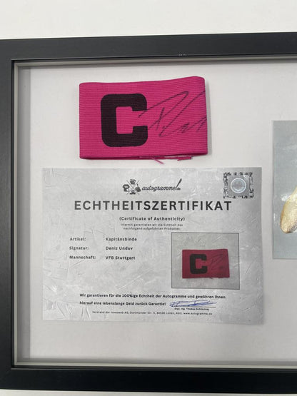 Brazalete de capitán firmado por Deniz Undav en un marco de autógrafos del VfB Stuttgart.