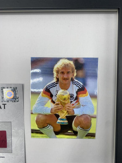 Brazalete de capitán firmado por Rudi Völler en un marco de autógrafos con temática alemana.